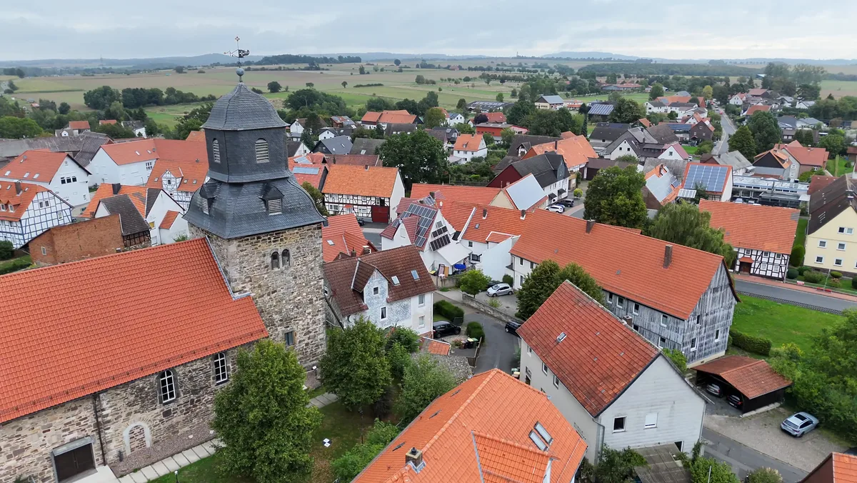 Kirchturm von Hohenkirchen mit geschieferter Haube, dahinter Fachwerkhäuser, Felder und Hügel