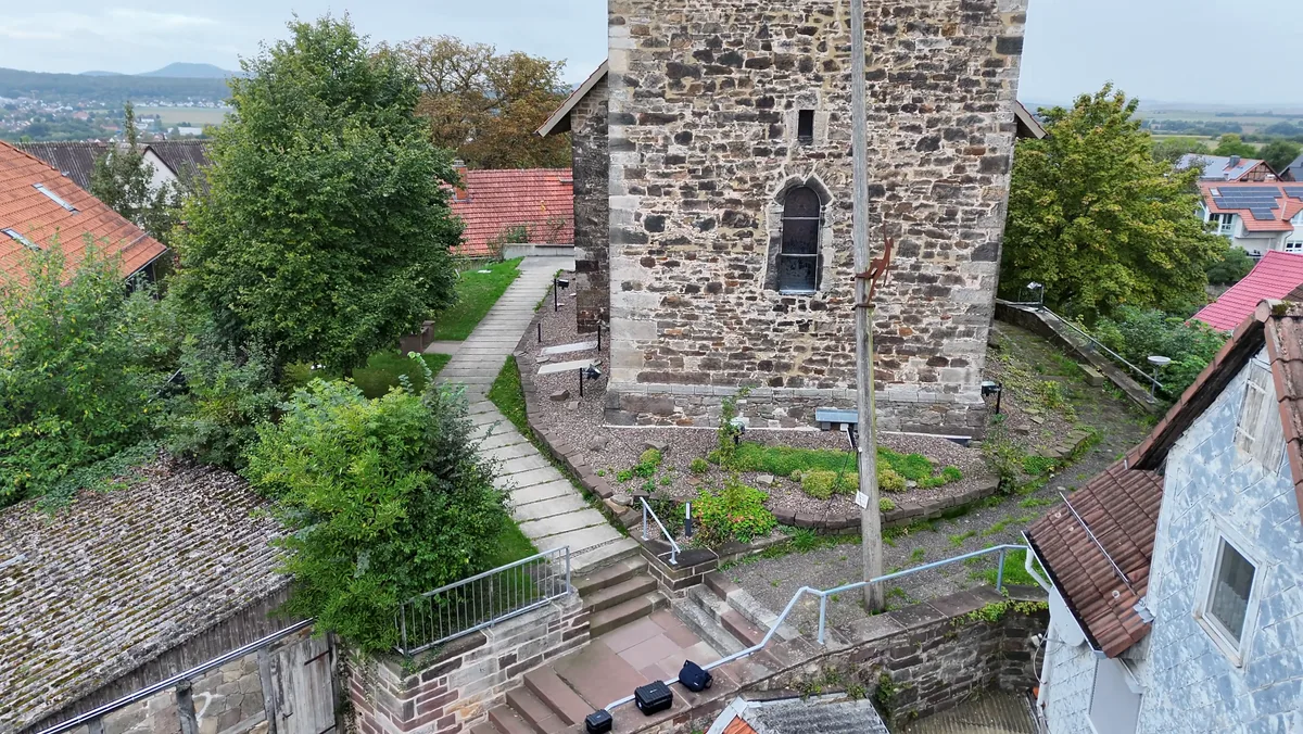 Bruchsteinturm mit Treppe, Weg und Bäumen am Fuß, daran der Stamm mit der Figur des Kirchenstürmers